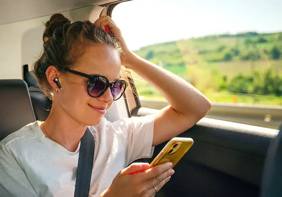Tronsmart Bluetooth Earphones, black wireless in-ear earbuds worn by a woman using a smartphone in a car