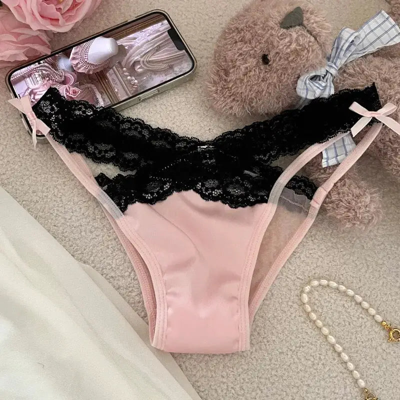 Pink satin thong with black lace waistband and sheer mesh sides, bow accents.