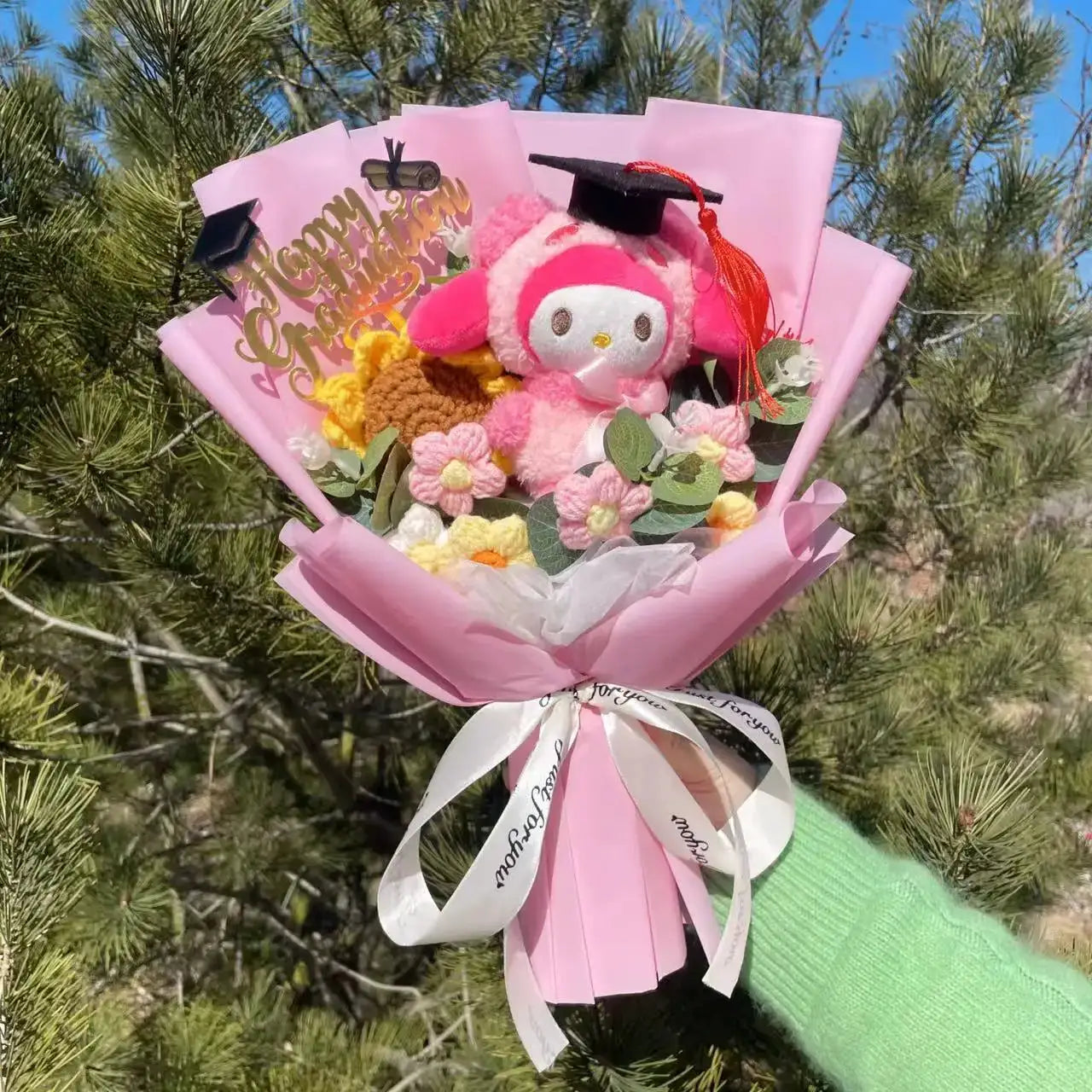Stuffed plants bouquet with pink wrapping, plush Hello Kitty wearing a graduation cap, yellow yarn flowers