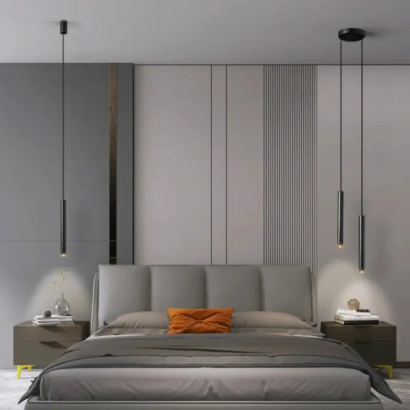 Minimalist bedside pendant lamps, two black cylindrical metal pendants with warm glow over a modern grey bed.
