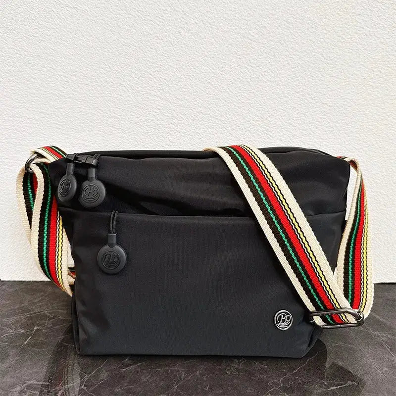 Ultra-light nylon crossbody bag by Simples Market, black with an adjustable wide multicolor striped strap and zipper closures.