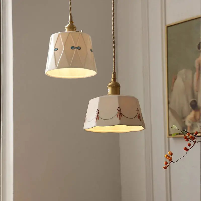 Two white ceramic pendant lights with brass-glazed finishes and printed patterns.