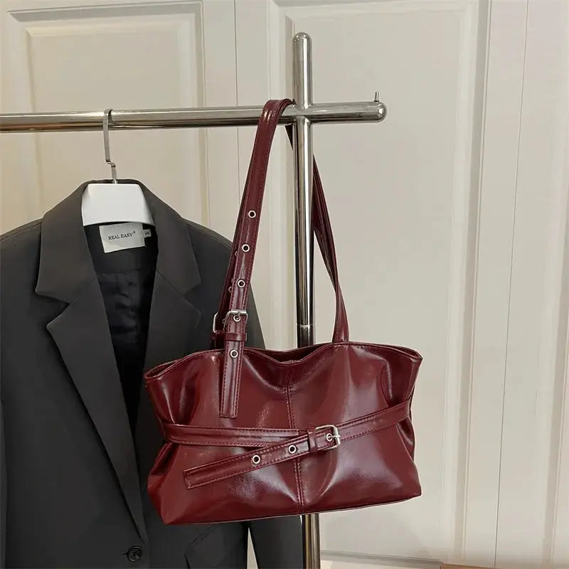 Handbag and gray blazer on a clothing rack; burgundy soft leather bag with belt buckle straps