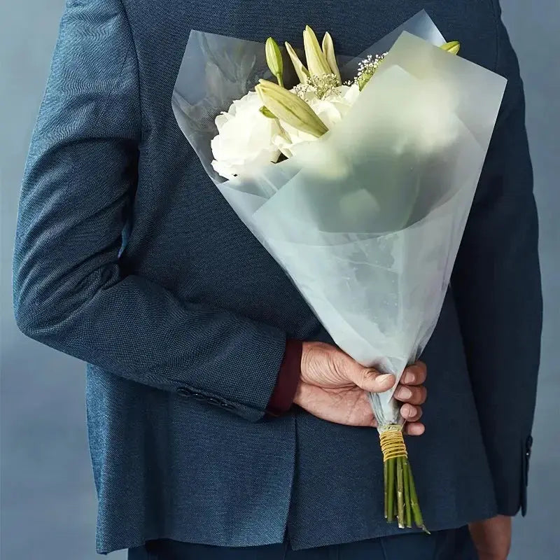 Bouquet of white flowers wrapped in translucent paper, held by a person in a dark blue suit.