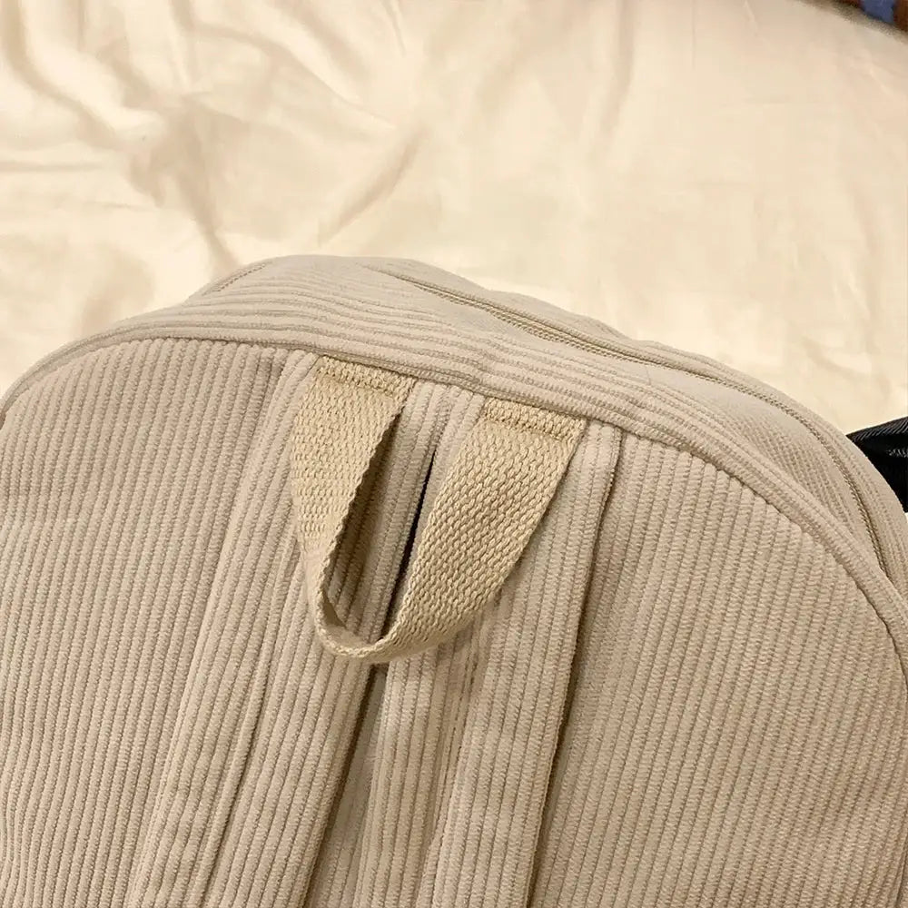Beige corduroy backpack with a top loop handle, perfect for commuting and college use.