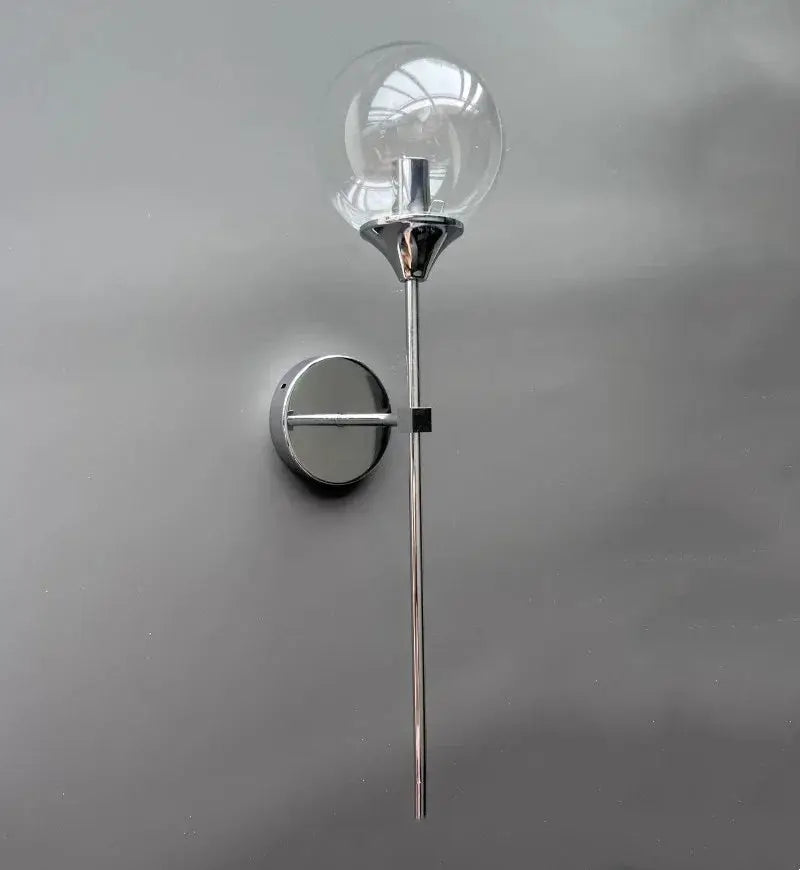 Modern glass wall lamp; chrome circular sconce with vertical stem and clear bulb.