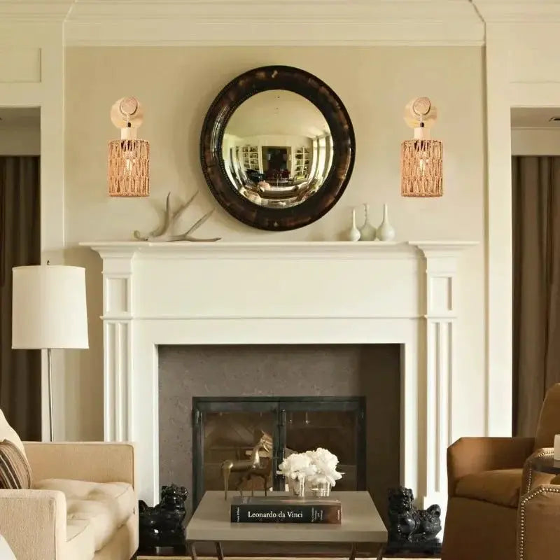Hemp rope wall lamps, cylindrical shades, pair by Simples Market flanking a round mirror above a white fireplace.
