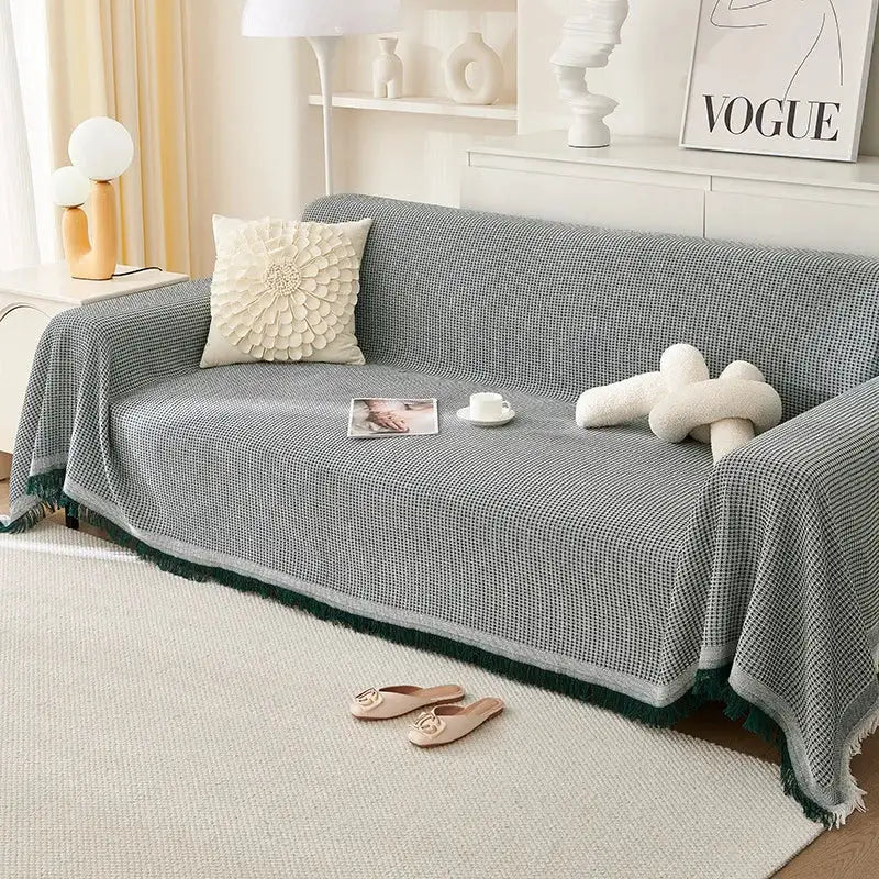Sofa throw blanket, grey knit with green fringe, draped over a living room sofa.