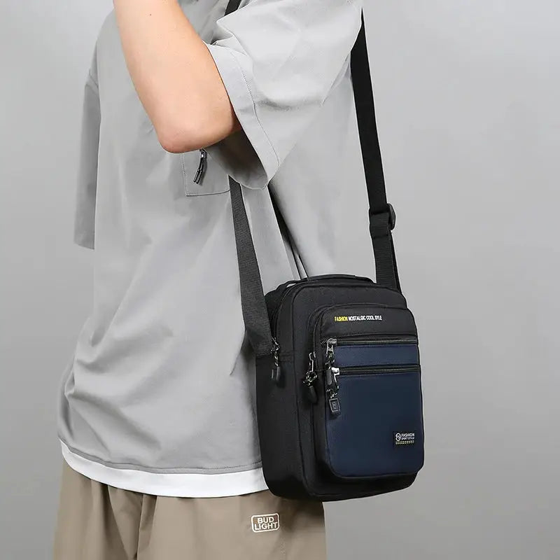 Men's crossbody bag with multiple pockets, black with navy front pocket.