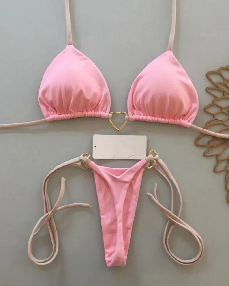 Two-piece pink halter bikini set with triangle cups and gold heart ring detail; thong-style bottom.