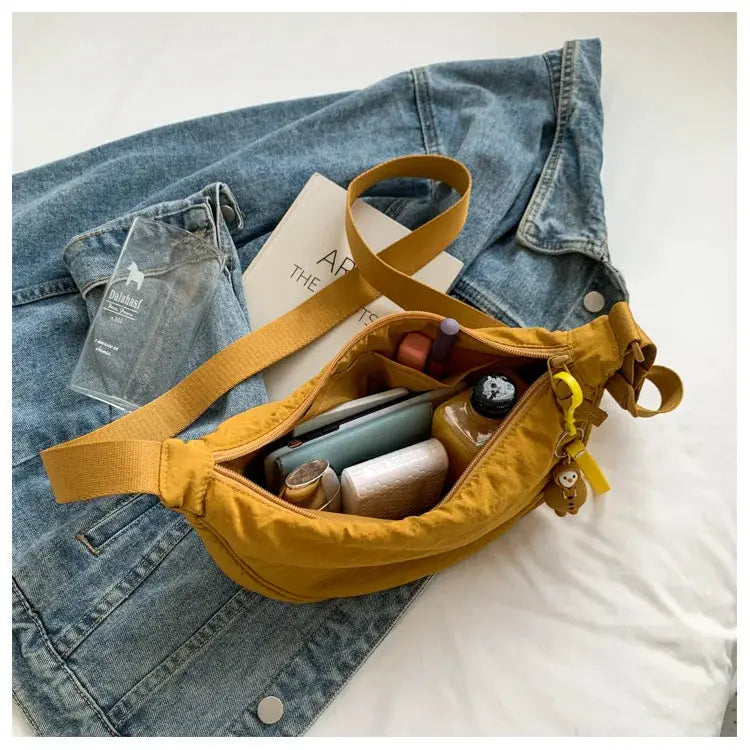 Crossbody bag by Simples Market in mustard nylon with padded strap, opened to reveal cosmetics, phone and keys.