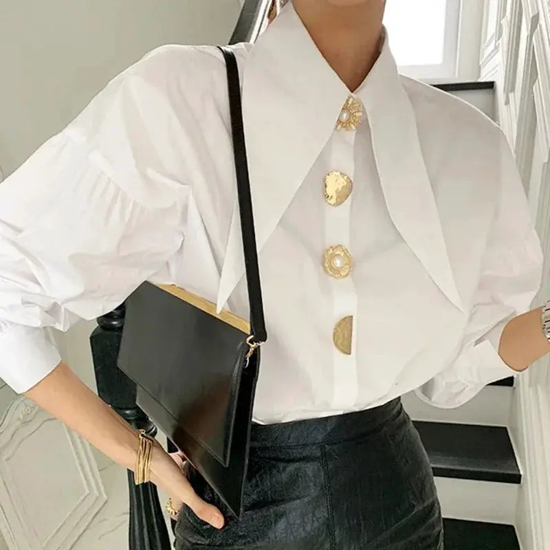 White loose long-sleeve blouse with sharp corner collar and gold-tone pearl buttons, paired with a black crossbody bag