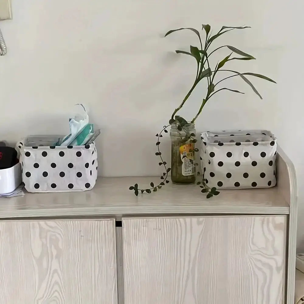 2 small foldable canvas storage baskets with handles, white with black polka dots, on a light wooden dresser