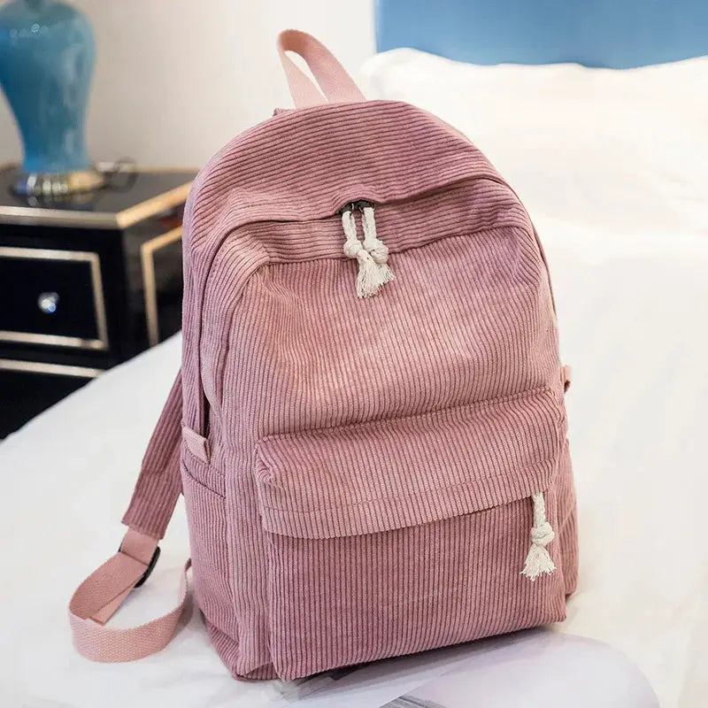 Pink corduroy kids backpack with front pocket, white tassel zipper pulls, and adjustable straps.