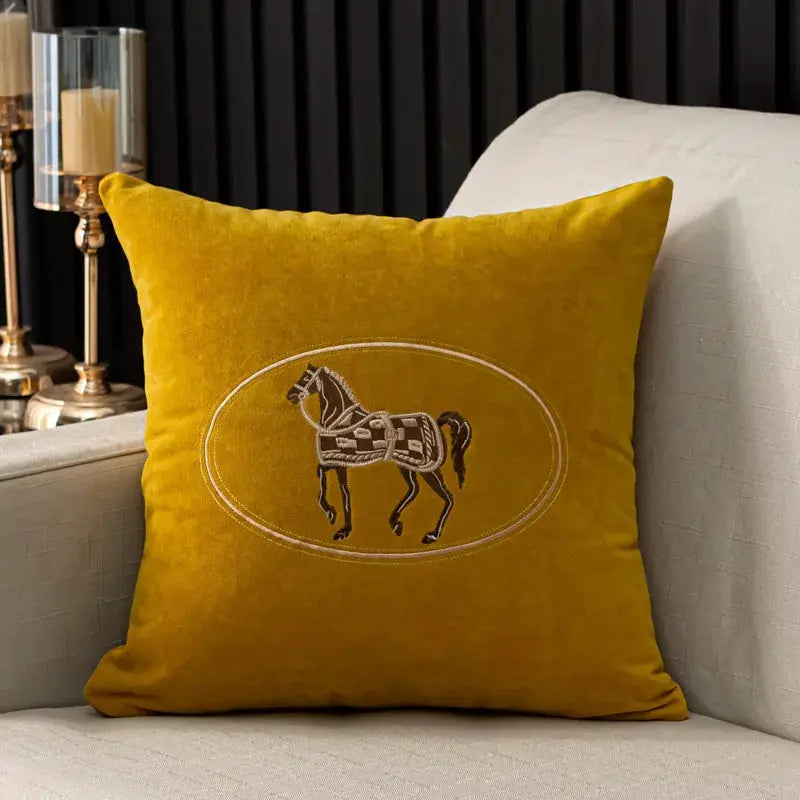 Cushion cover in mustard-yellow with an embroidered horse inside an oval frame.