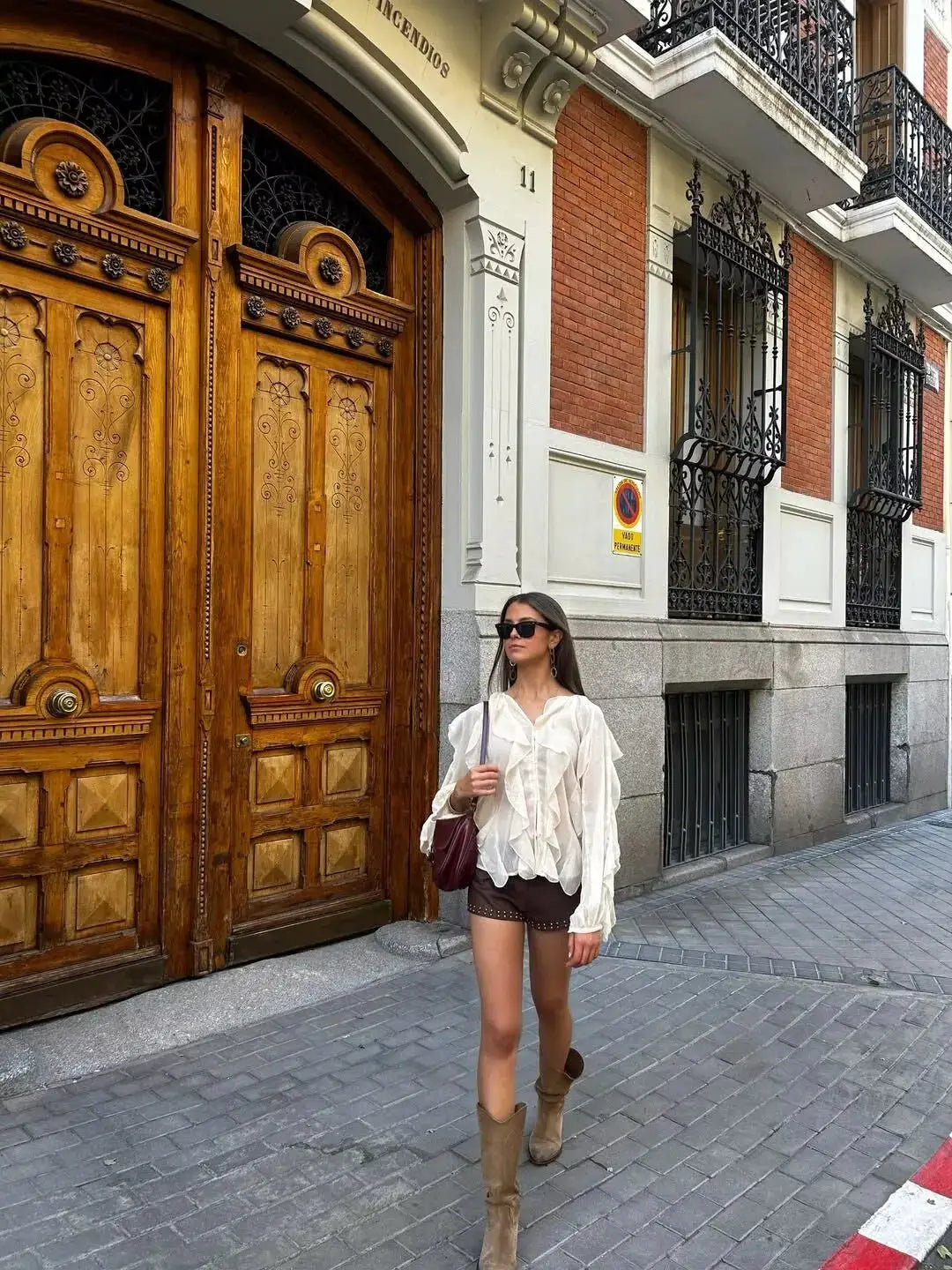 Women's white semi-sheer ruffle blouse with long sleeves and front buttons, street-style look with sunglasses.
