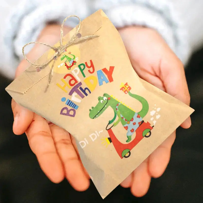 Kraft paper gift bag with rainbow dinosaur on a scooter and Happy Birthday print, tied with twine, held in hands.