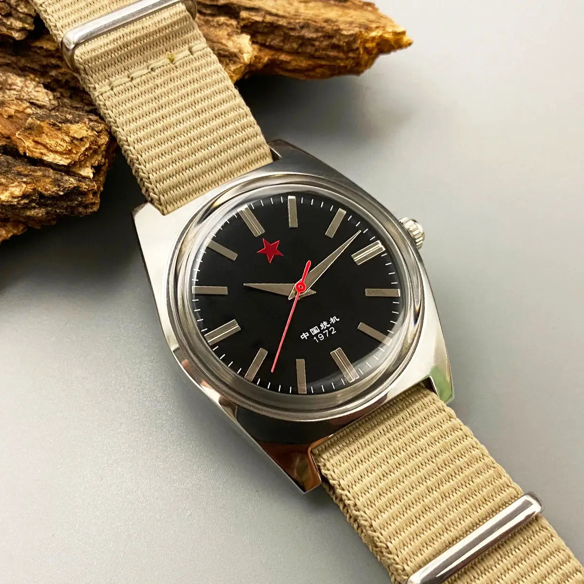 Mens mechanical watch with black dial, red star logo, silver case and beige fabric strap.