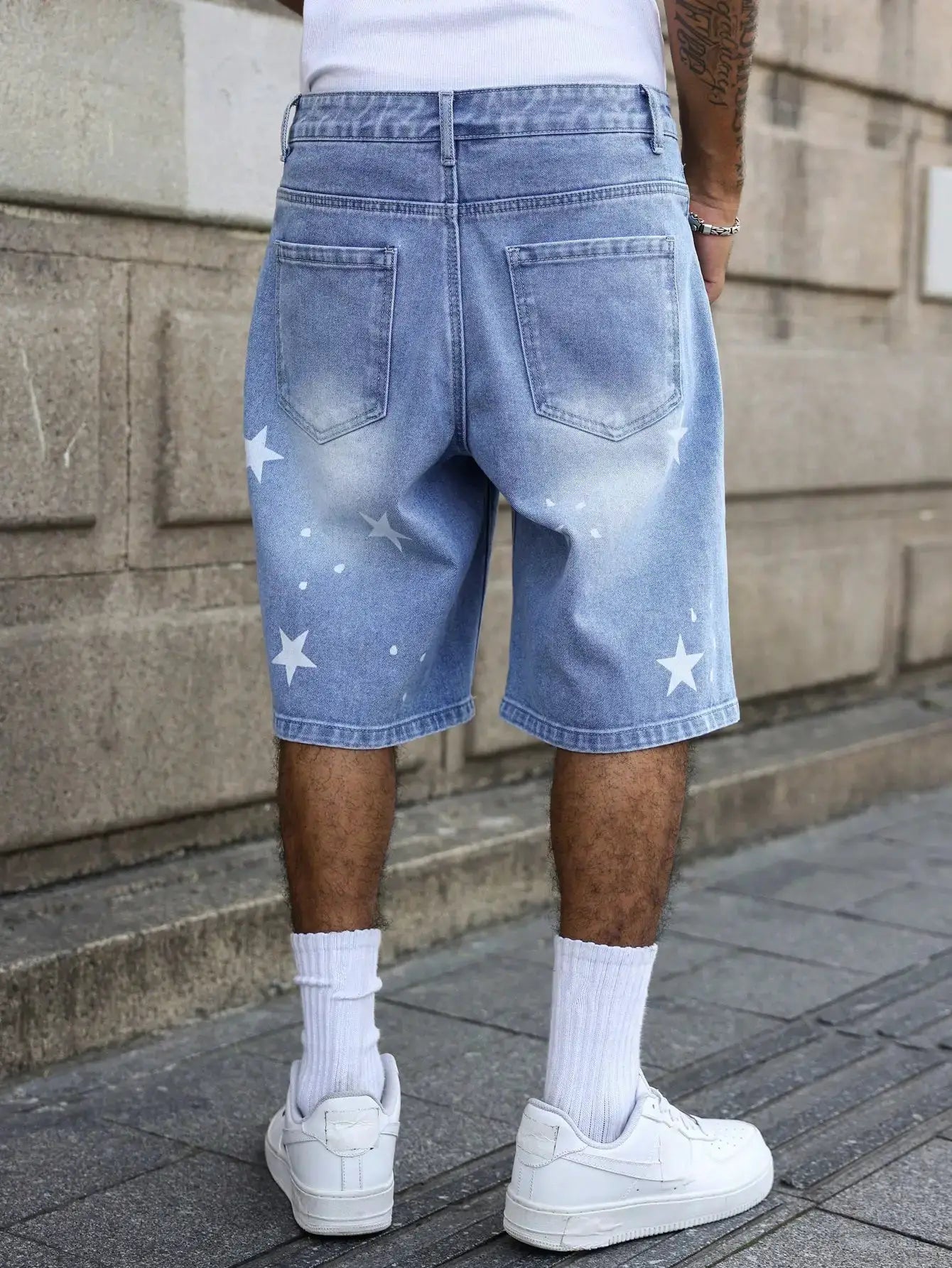Men's blue denim shorts with white star prints on the lower legs, back pockets, knee-length.