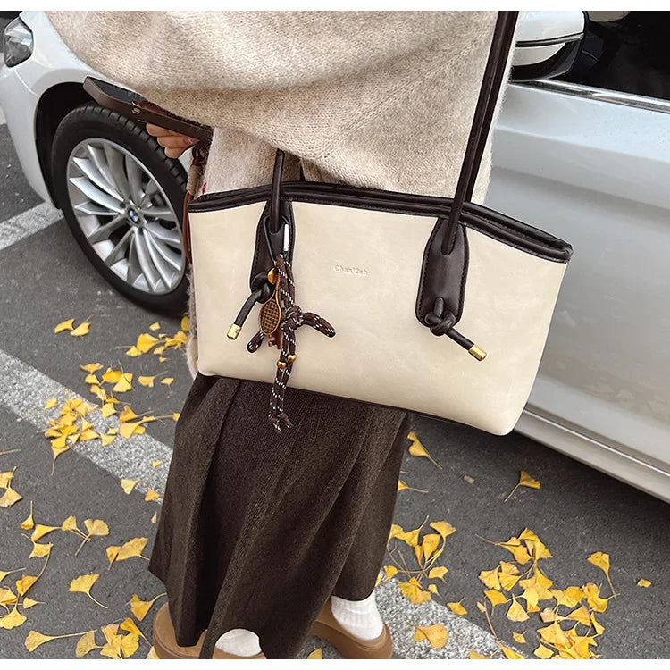 Simples Market PU leather shoulder bag in beige with dark brown trim and double handles, tassel charm.