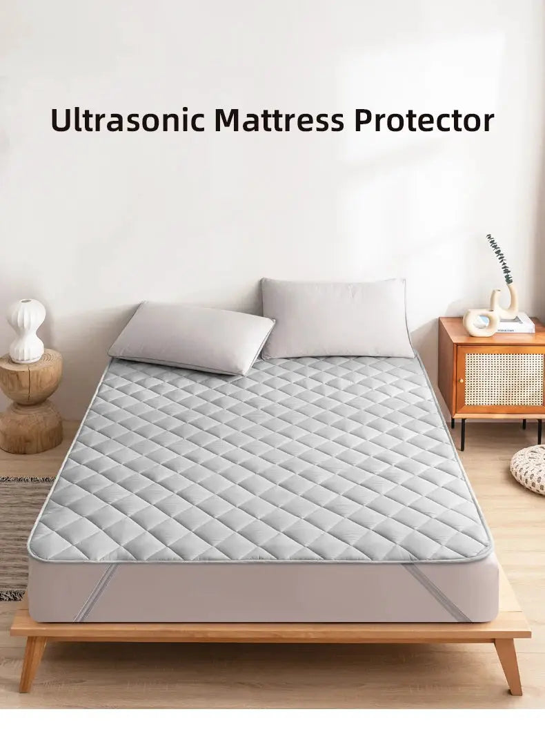 Ultrasonic Mattress Protector by Simples Market; light gray quilted cover with elastic band on a bed