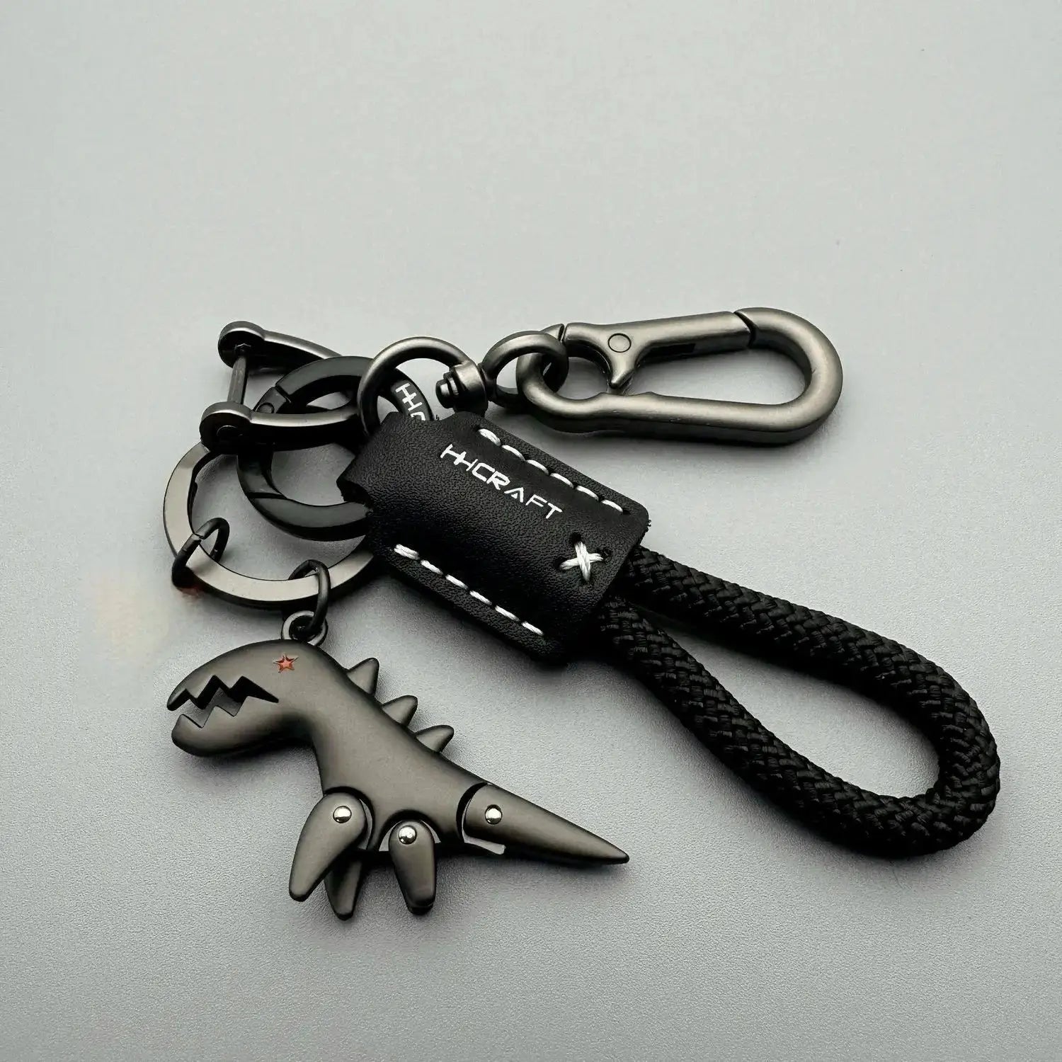 Keychain with black woven rope, metal carabiner clip, leather tag marked HCRAFT, dinosaur charm