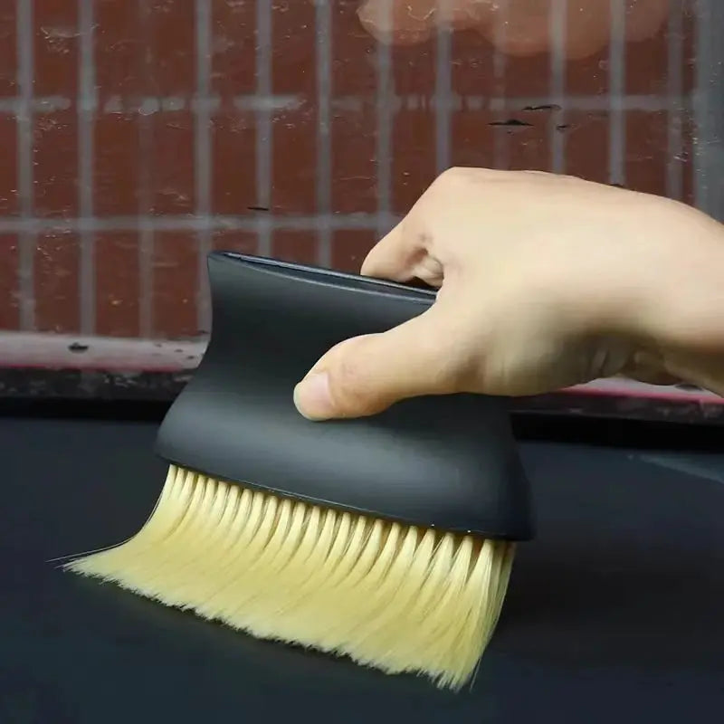 Car interior dust brush with soft yellow bristles and black curved handle for cleaning gaps and air vents.