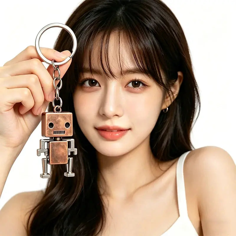 Retro movable robot keychain in copper-toned metal, square robot pendant with arms and legs on a ring held by a woman