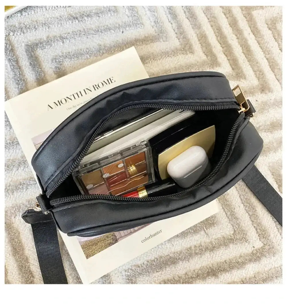 Black PU leather shoulder bag with crossbody strap, zipper open to reveal makeup and small items inside