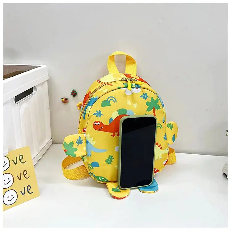 Yellow children's backpack with cartoon dinosaur print and top handle, featuring a phone in the front pocket.