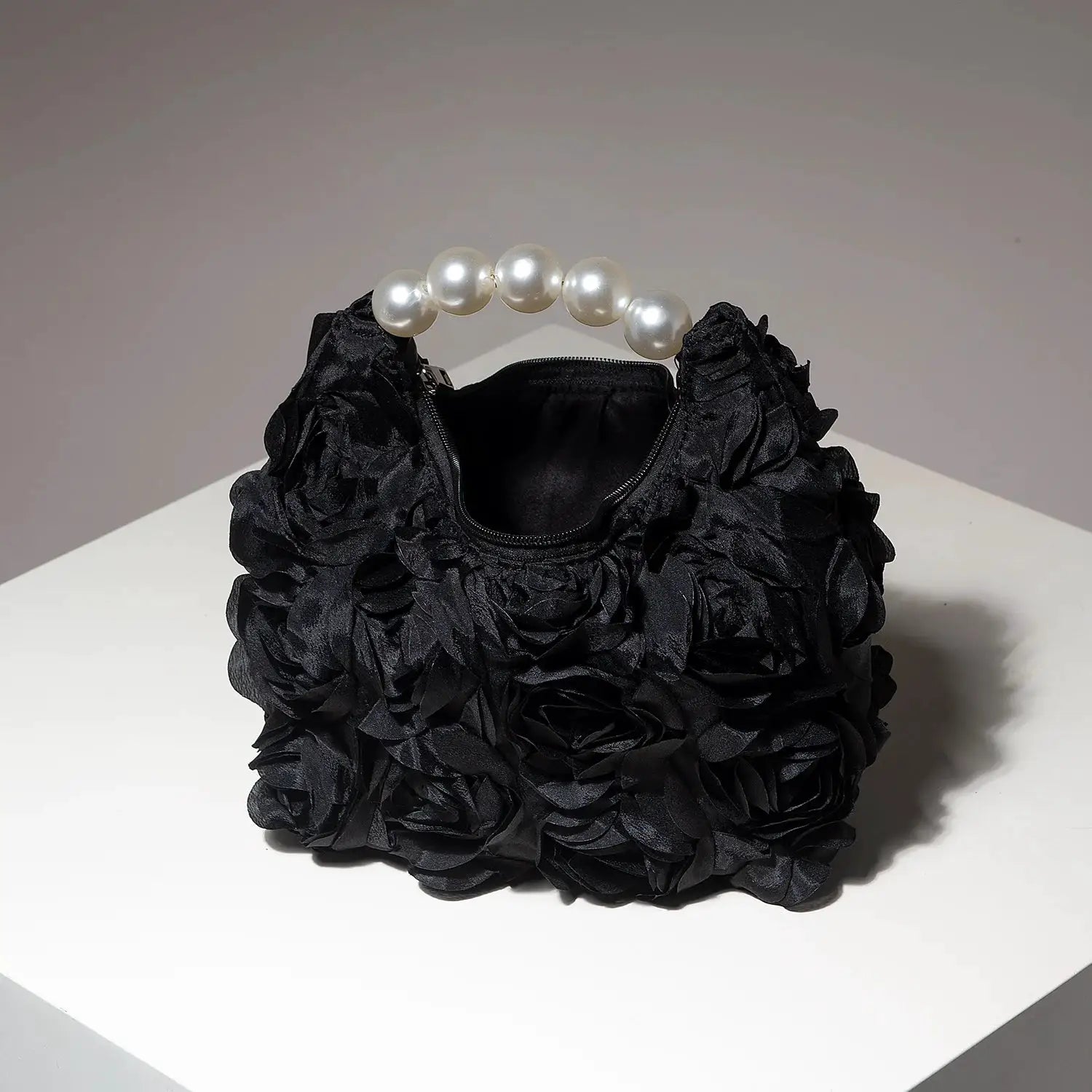 Black pearl-handled handbag with a textured floral, ruffled surface and zip closure.