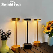 Three aluminum LED desk lamps in gold and black with warm light on a wooden table, Shenzhi Tech logo visible.