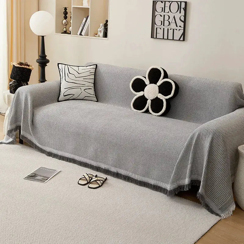 Gray knitted sofa throw blanket with fringe on a sofa, two decorative cushions