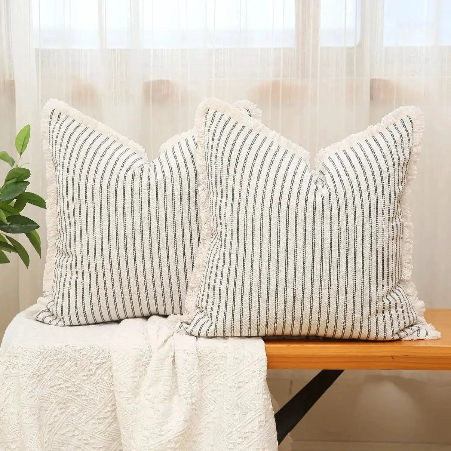 Wool striped cushion covers with fringe; pair of white covers with navy vertical stripes on a wooden bench
