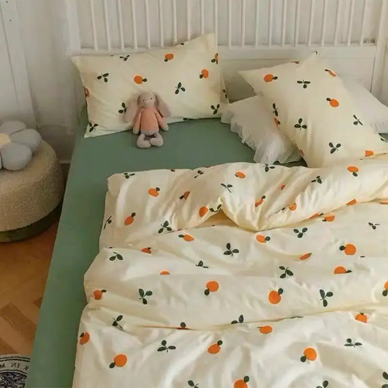 Bedding set: cream duvet cover with orange fruit and green leaf pattern, matching pillowcases on a green sheet