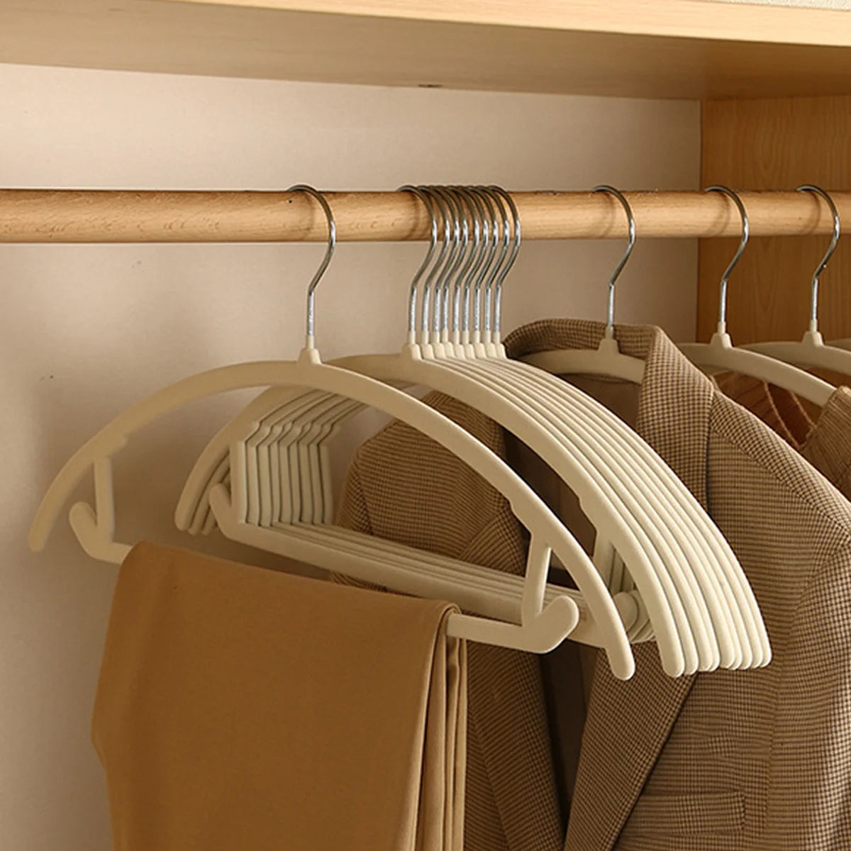 White plastic clothes hangers with metal hooks on a wooden closet rod.