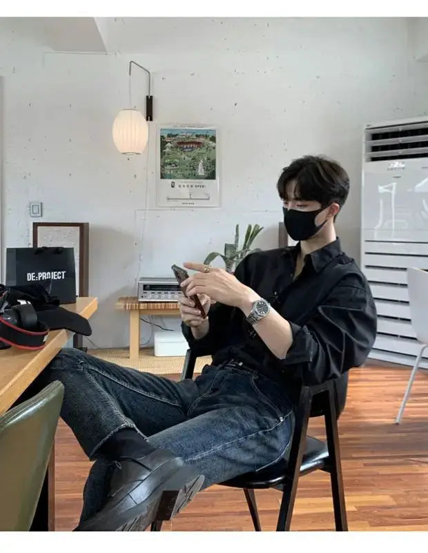 Men's black solid-color long-sleeve shirt worn by a man seated at a desk using a smartphone