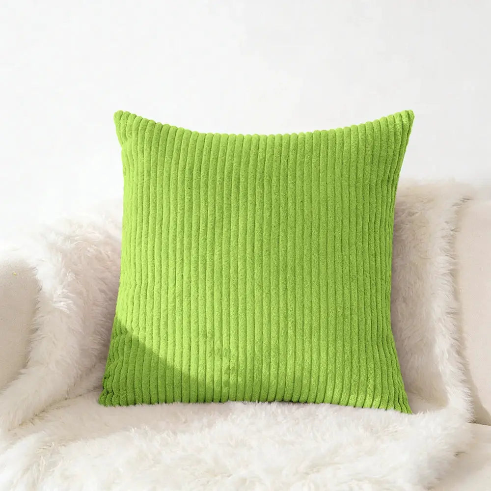 Corduroy pillow cover in lime green with vertical ridges, placed on a white fluffy throw.