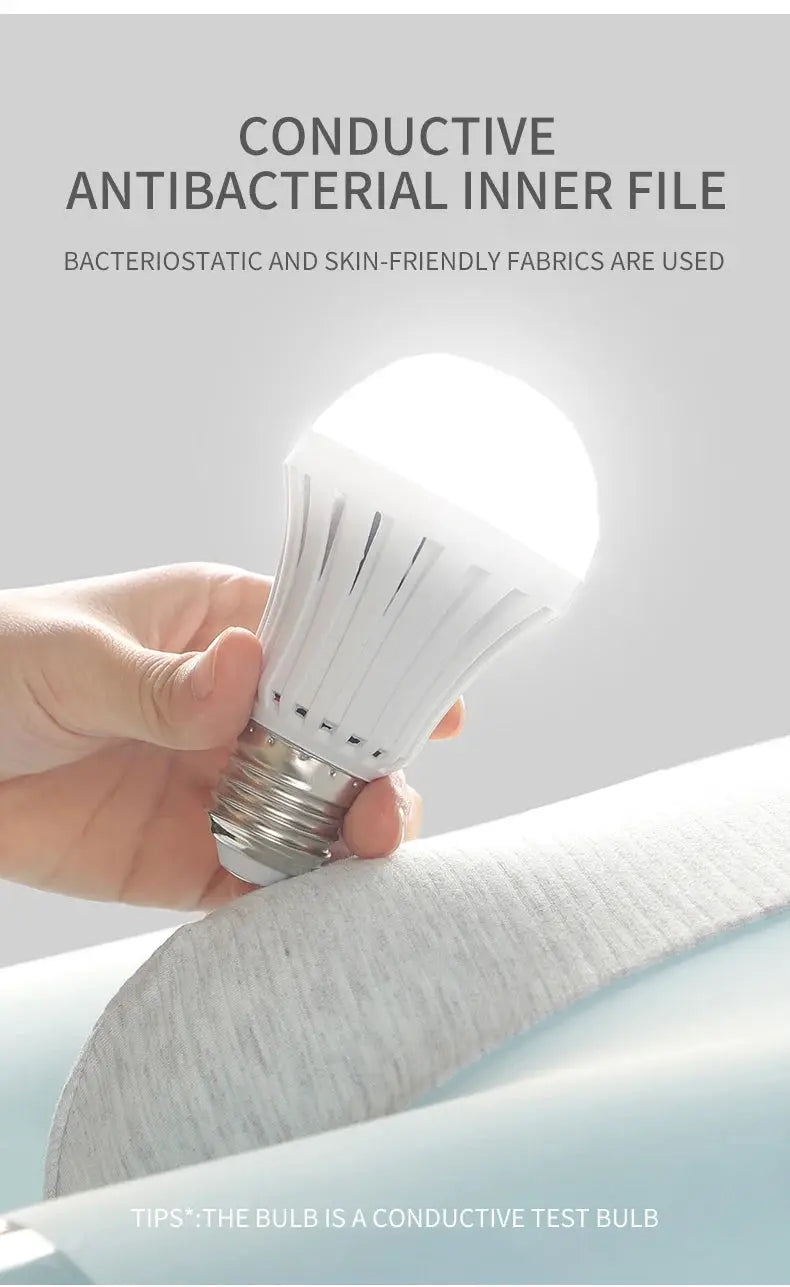LED light bulb with white plastic fins and screw-base, held in hand over soft fabric background, close-up view.