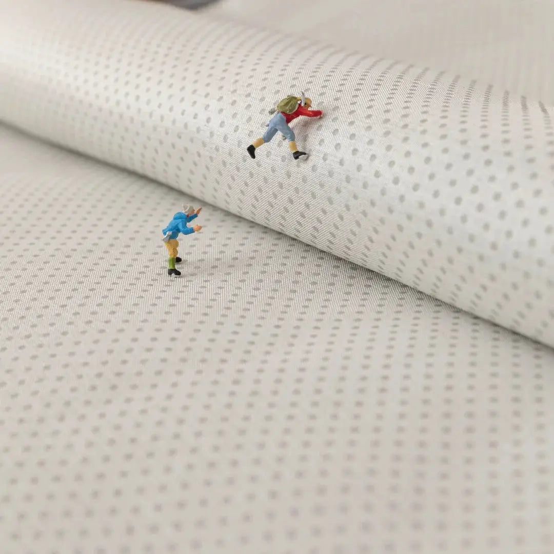 Sofa slipcover fabric close-up in white with a small gray dotted pattern; two tiny figurines on the material.