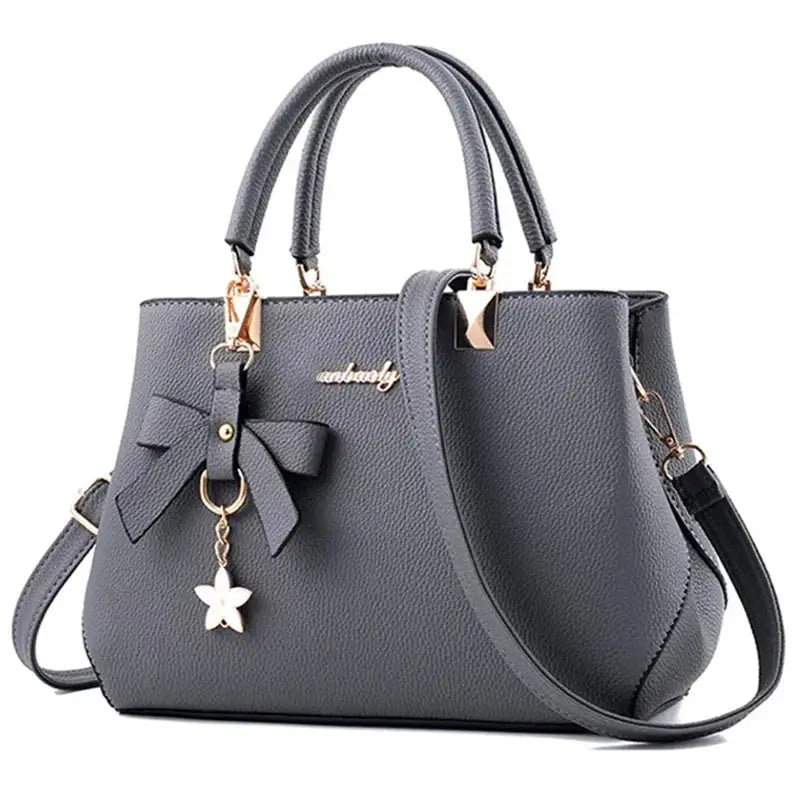 Women's gray crossbody handbag by Simples Market with double handles, bow charm and flower pendant.