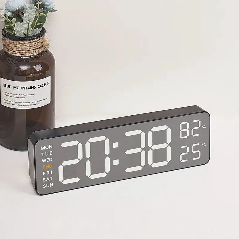 Mirror-brushed digital wall clock with large LED digits; shows day of week, humidity 82%, and temperature 25°C.
