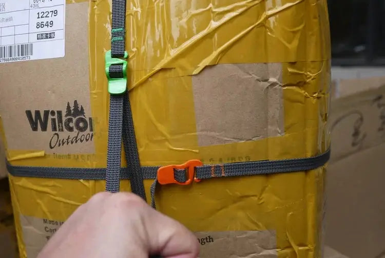 Simples Market camping luggage strap with orange quick-release buckle and green buckle on gray webbing securing a box