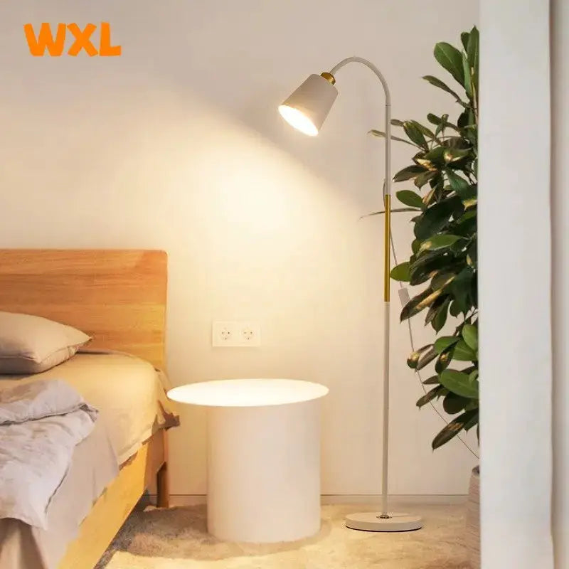 Simples Market floor lamp with adjustable metal head and white shade beside a white round table; WXL logo visible.
