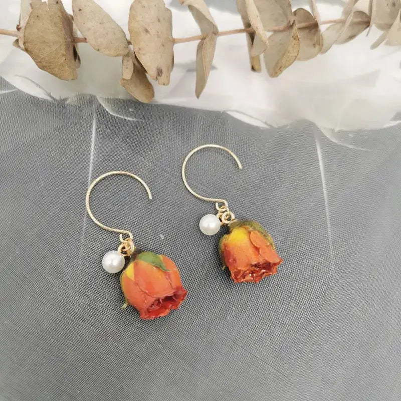 Two red rose epoxy resin drop earrings with a pearl accent and gold-tone hooks
