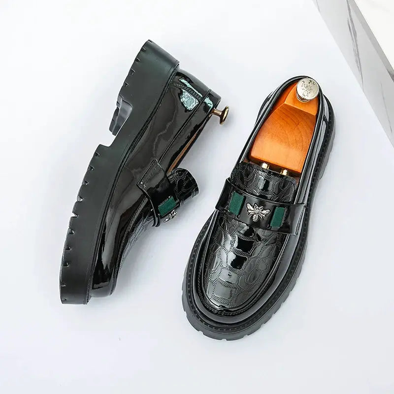 Two black patent leather loafers with thick chunky soles and bee-emblem strap for business or formal wear.