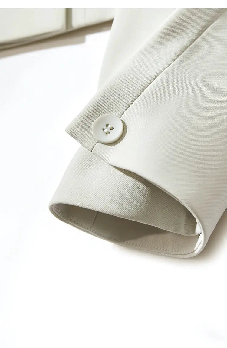 Cream blazer sleeve close-up with white button and subtle textured fabric