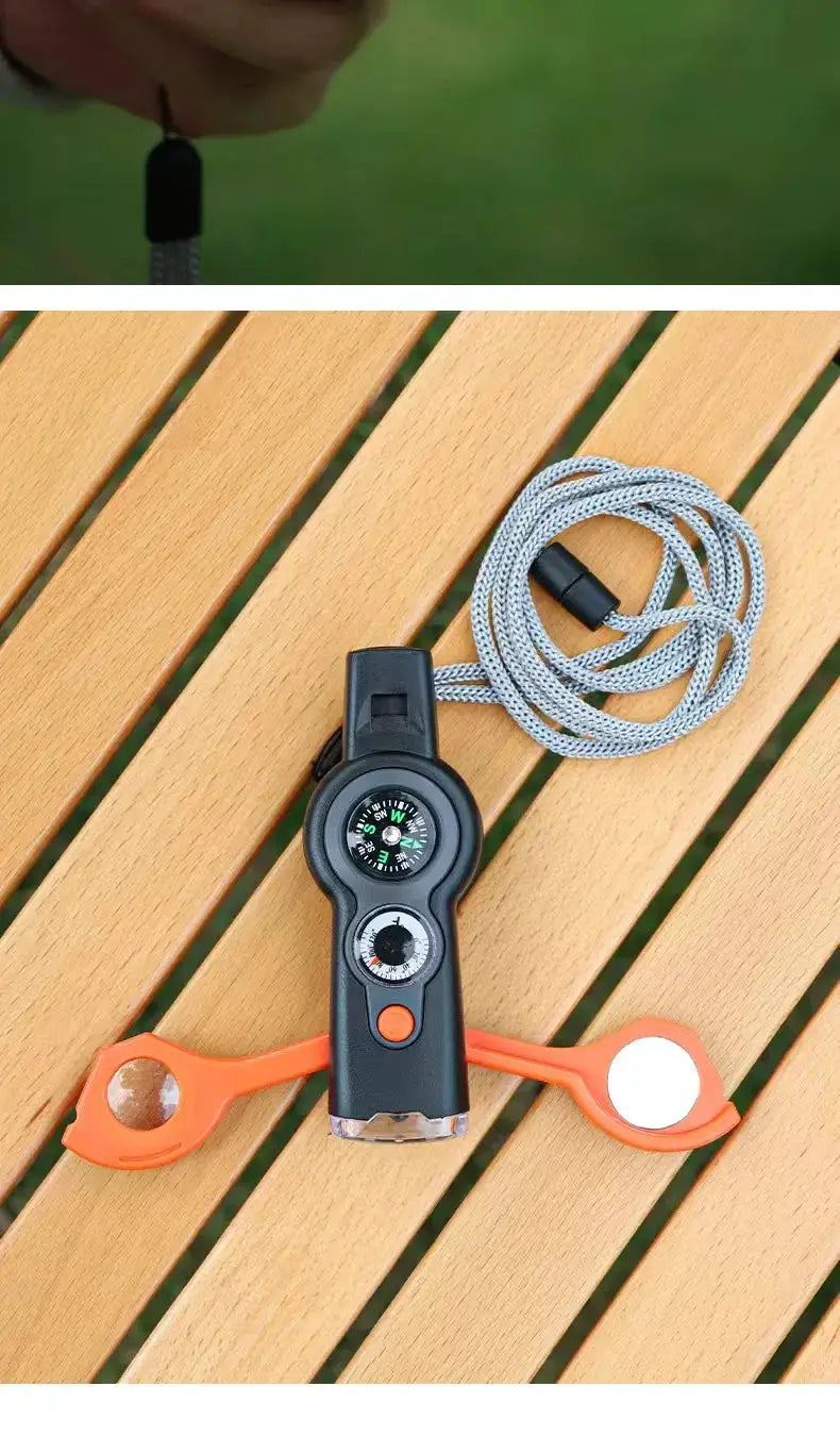 7-in-1 outdoor survival whistle with compass, black body, orange side wings, and gray lanyard by Simples Market