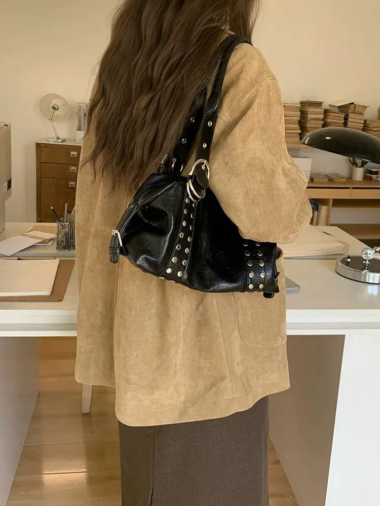 Black PU leather rivet shoulder bag with silver studs, worn by a woman in a beige suede jacket.