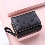 Women's black quilted wallet with zip closure, pink interior, and attached wrist strap.